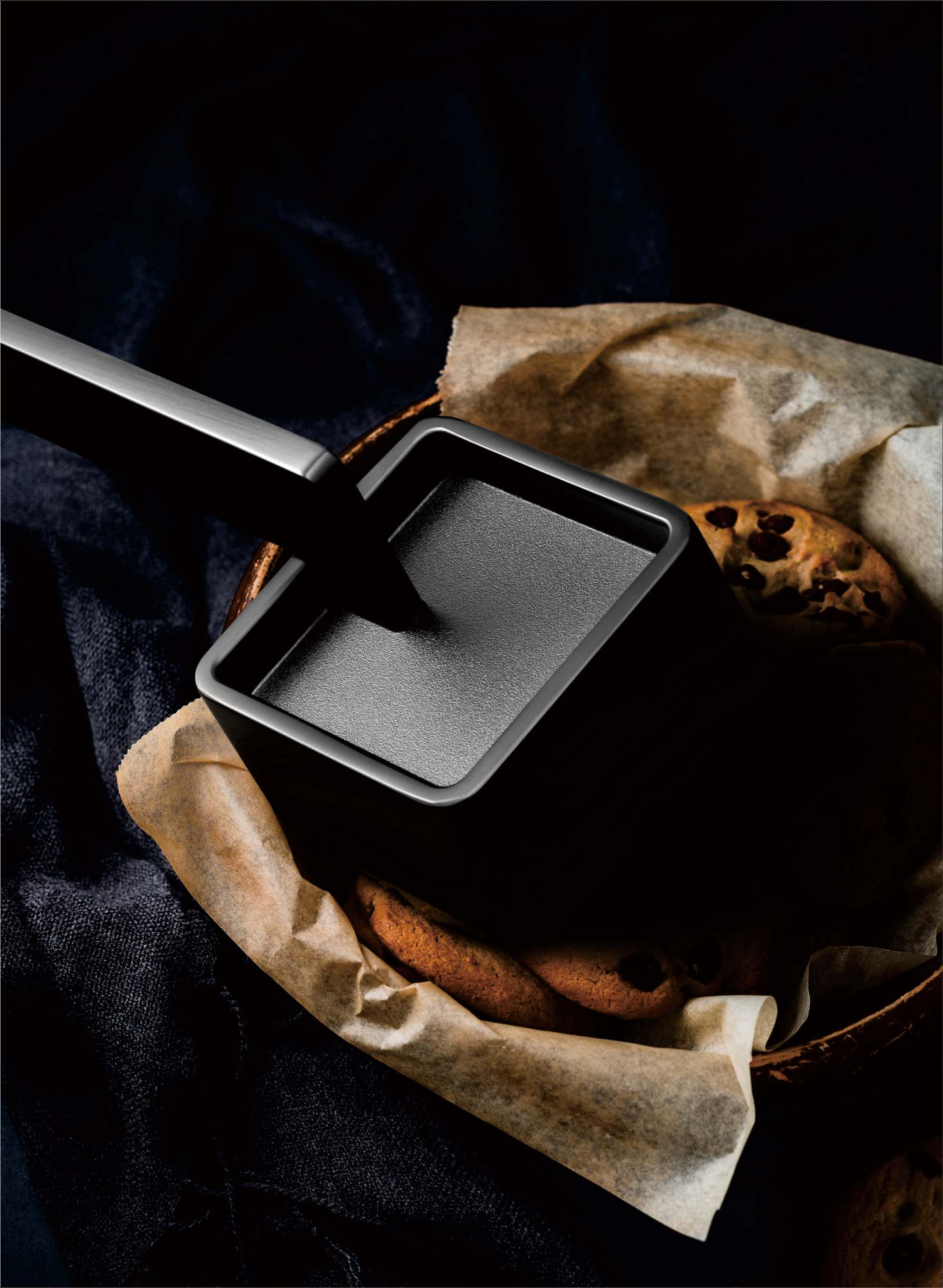 Black square pan on a dark surface with cookies and brown paper