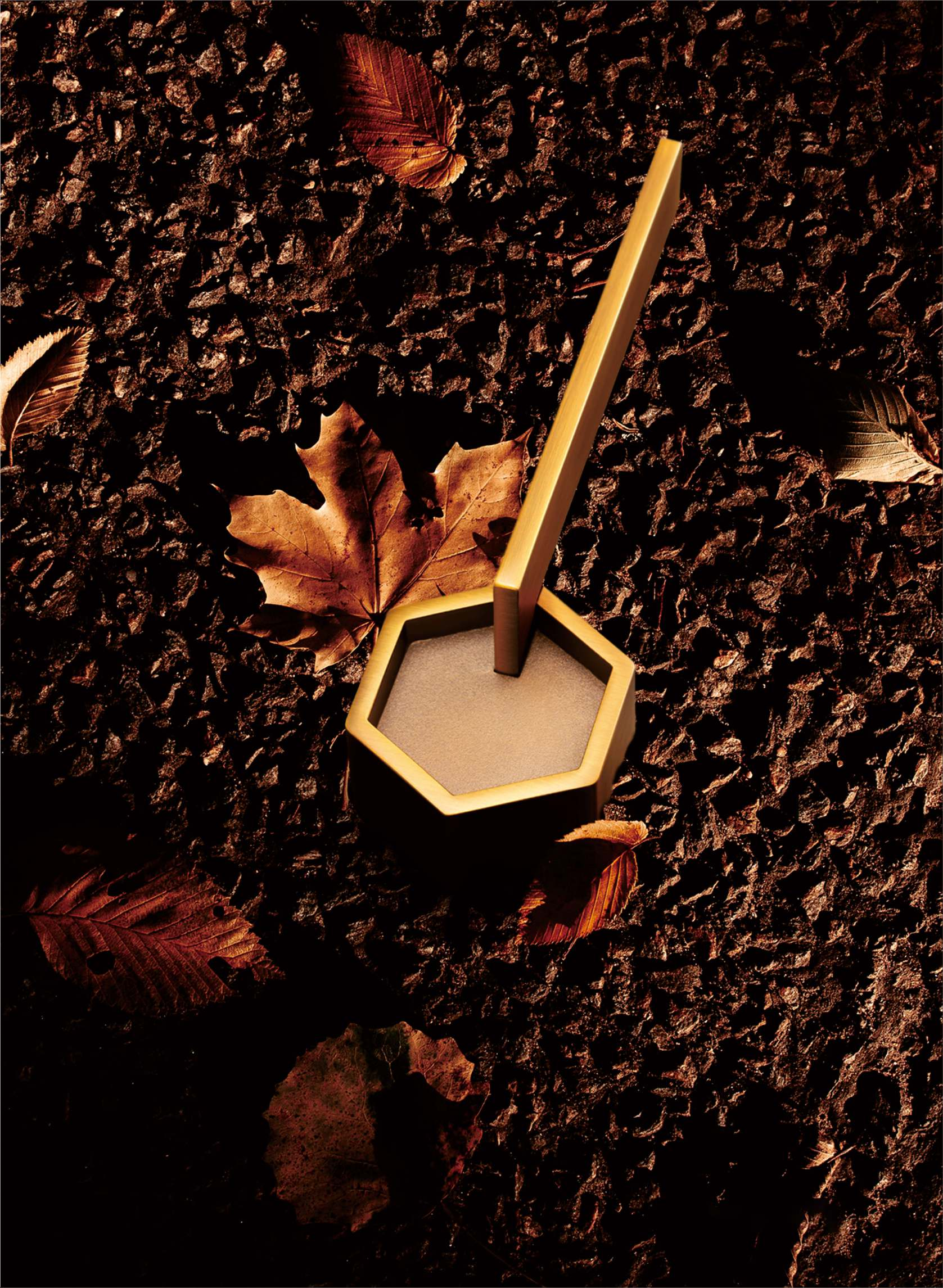 Hexagonal candle holder with a wooden stick on a textured brown surface with leaves